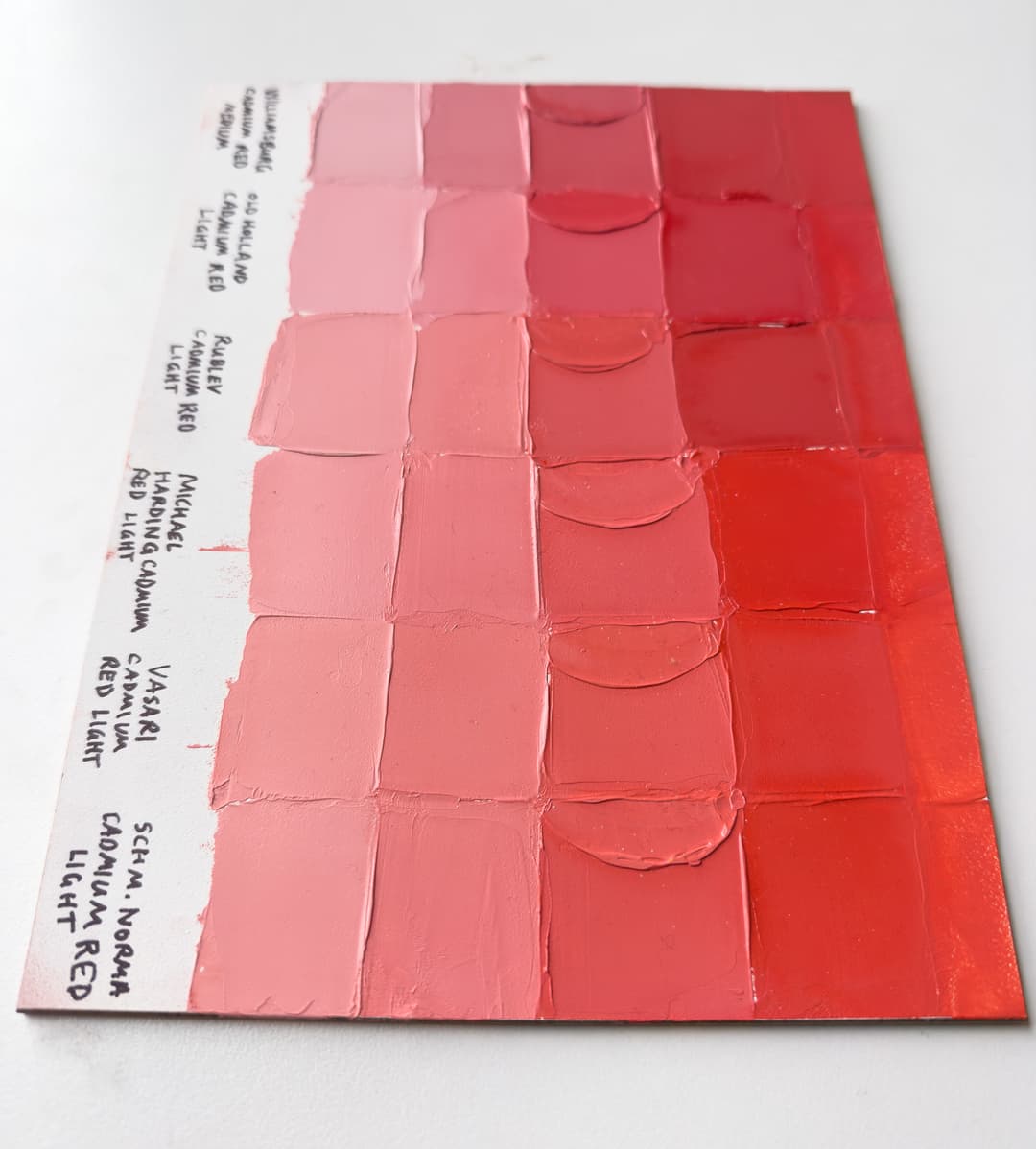 A painted panel showing six different red paints mixed with Titanium White
