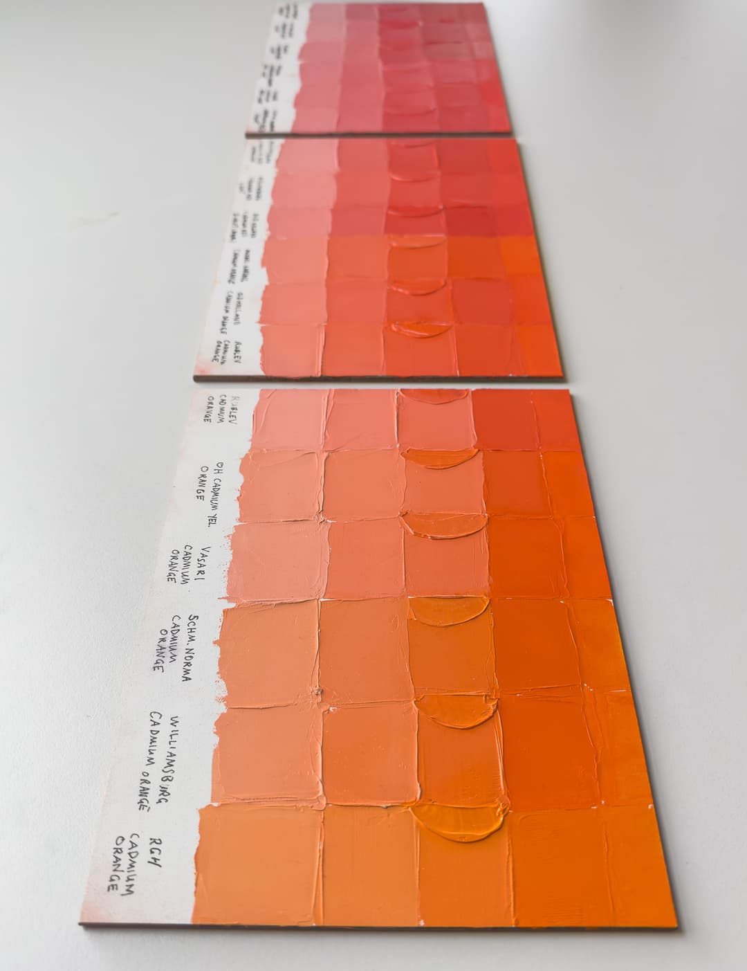 Orange paint swatches explore the differences between brands of Cadmium Orange. Three panels show orange color swatches ranging from yellow orange to red orange